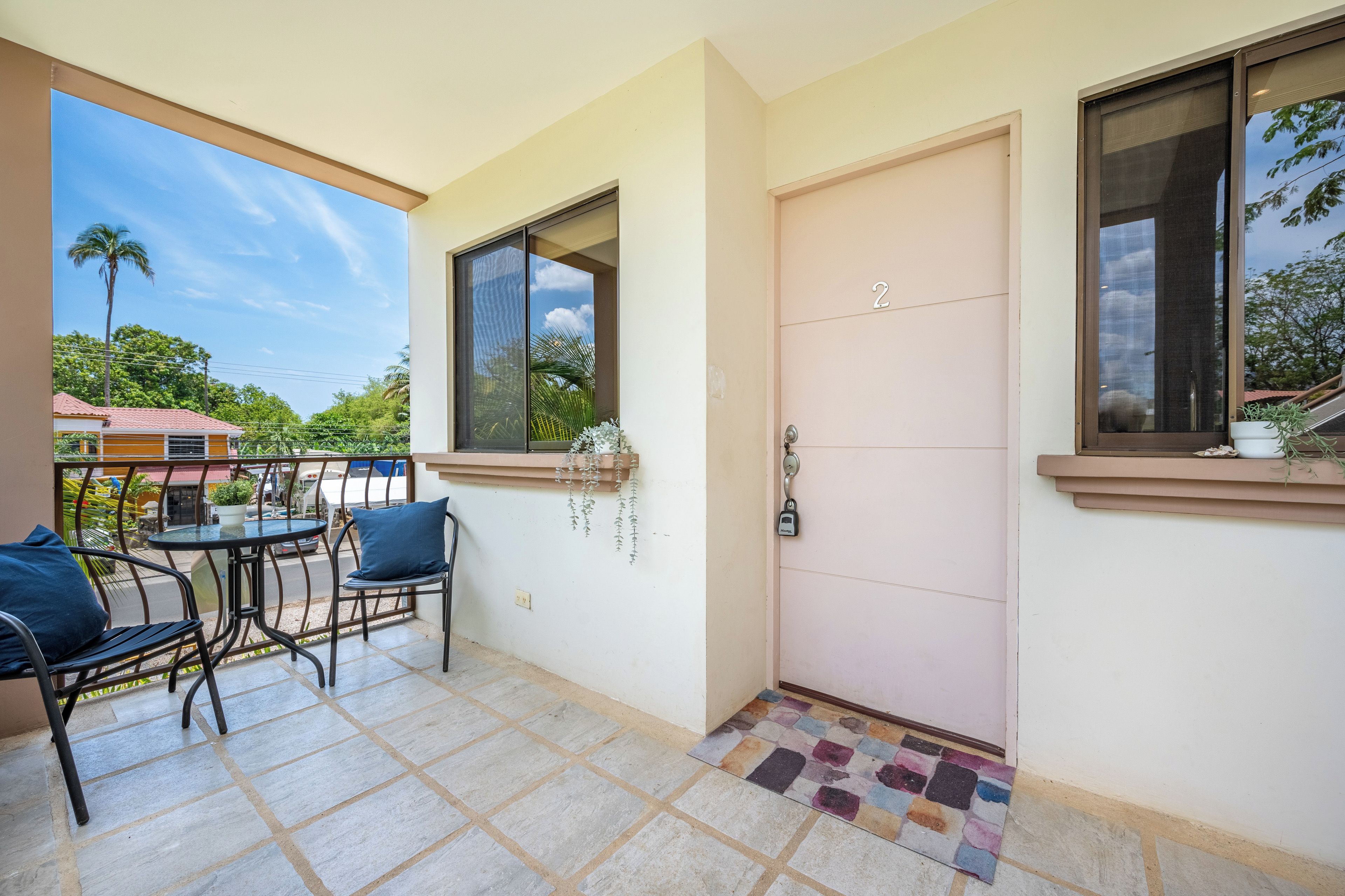 A balcony with a table and chairs, a door with a number, and a view of the outside.