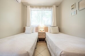 Ein Doppelzimmer mit zwei Betten, einem Nachttisch, einer Lampe und einem Fenster mit Vorhängen.