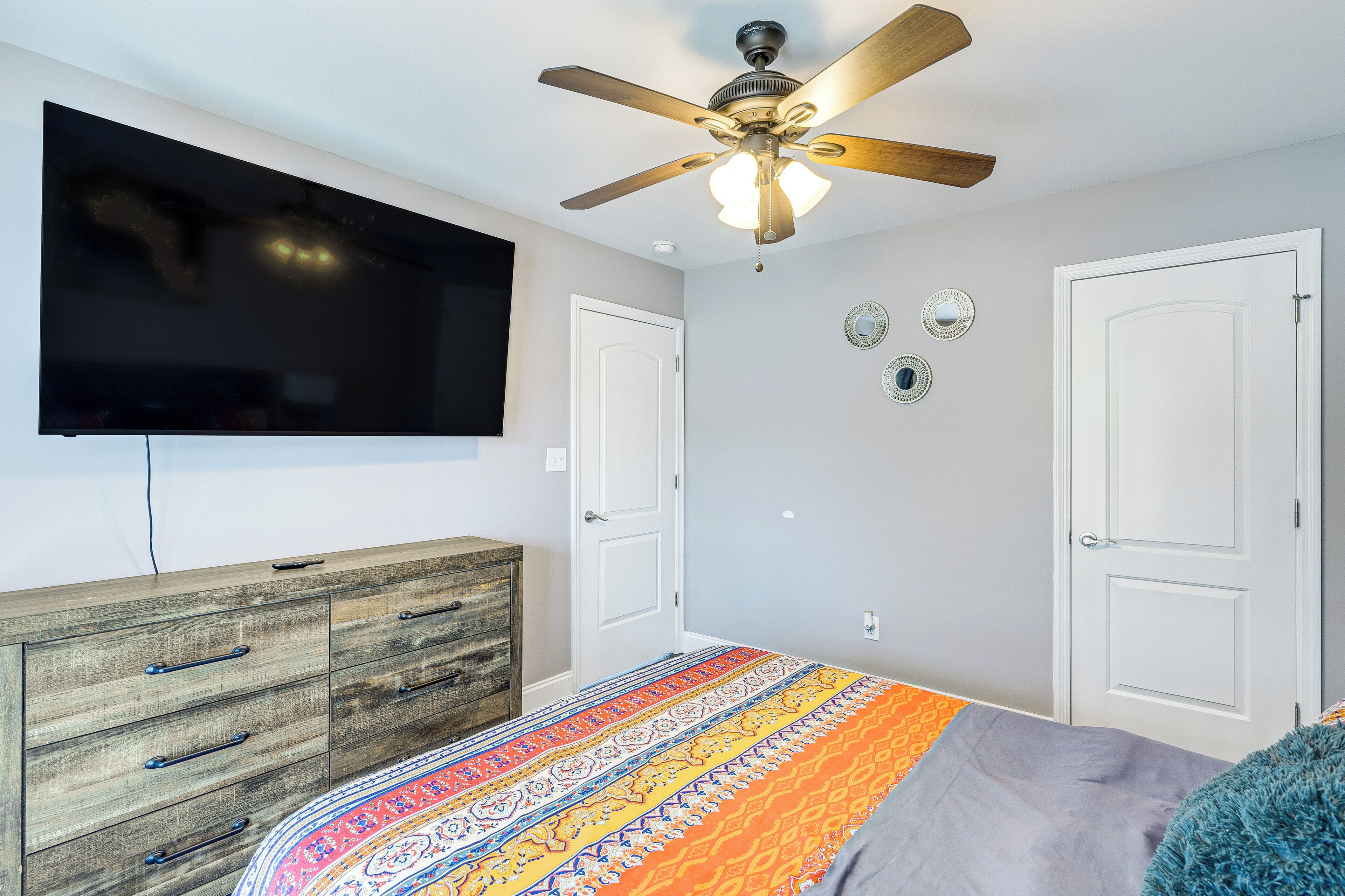 A bedroom with a bed, a ceiling fan, a TV, a dresser, and two doors.
