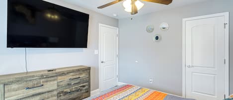 A bedroom with a bed, a ceiling fan, a TV, a dresser, and two doors.