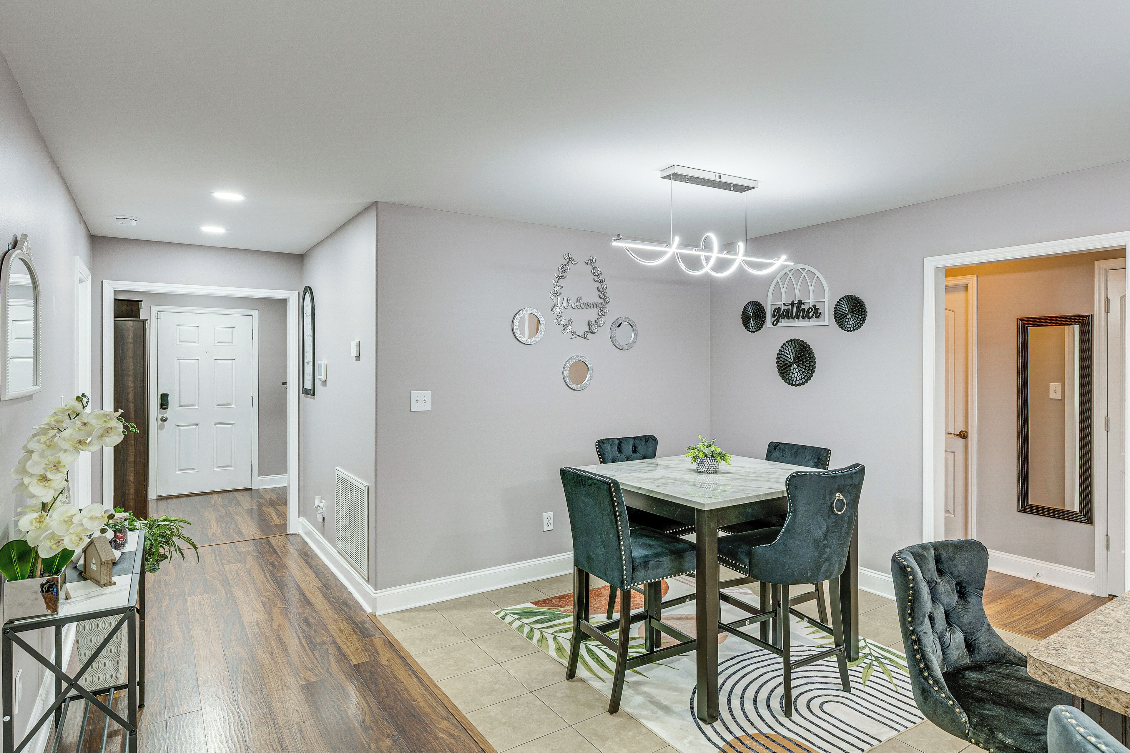 A dining area with a marble table and upholstered chairs, a decorative ceiling light, and wall-mounted mirrors.