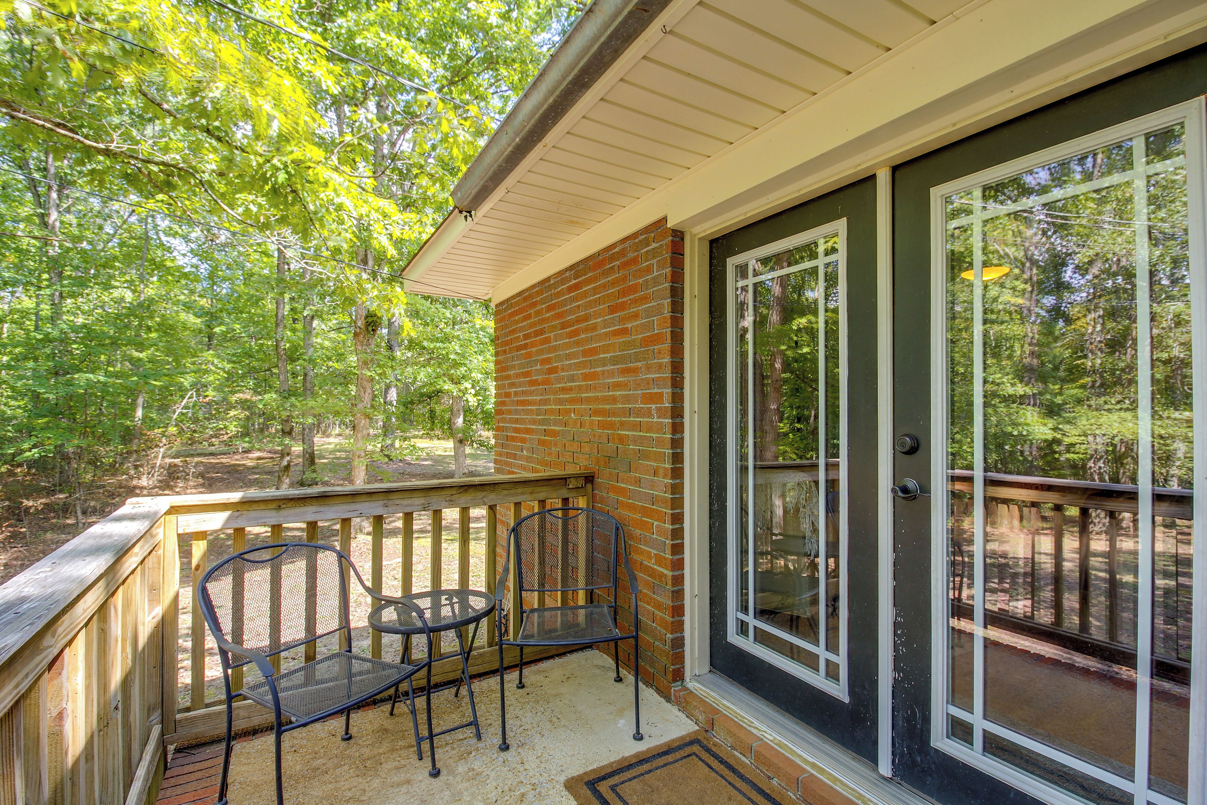 A covered porch with two metal chairs and a table, a brick wall, and a glass door leading to a deck.