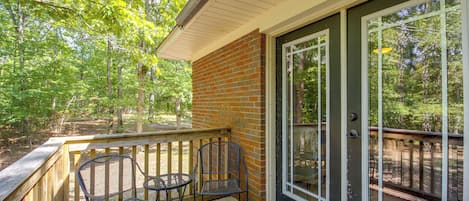 A covered porch with two metal chairs and a table, a brick wall, and a glass door leading to a deck.