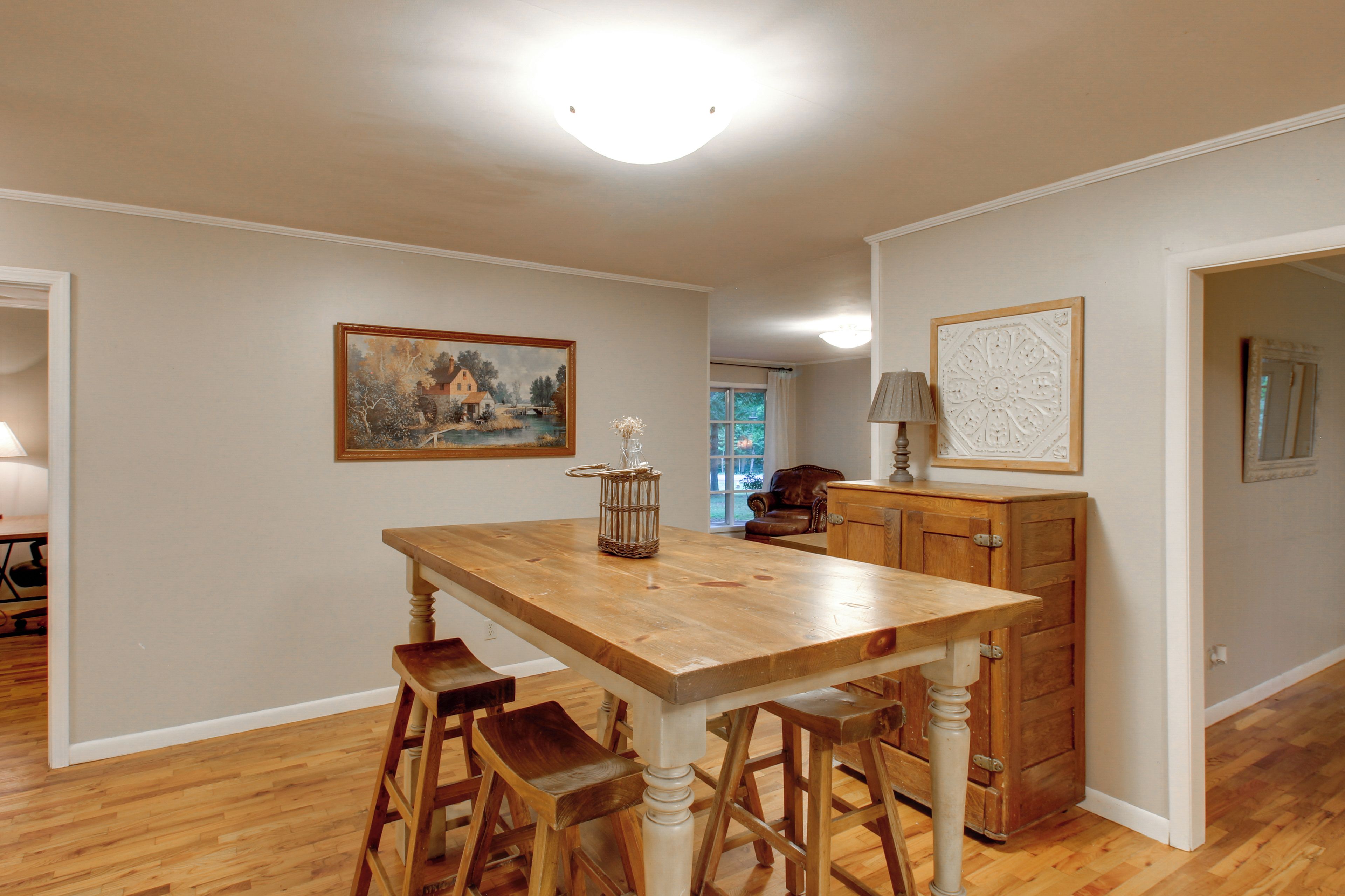 A dining area with a wooden table, bar stools, a painting, and a cabinet.