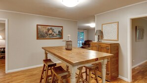 Uma sala de jantar com mesa de madeira, banquetas, um quadro e um armário.