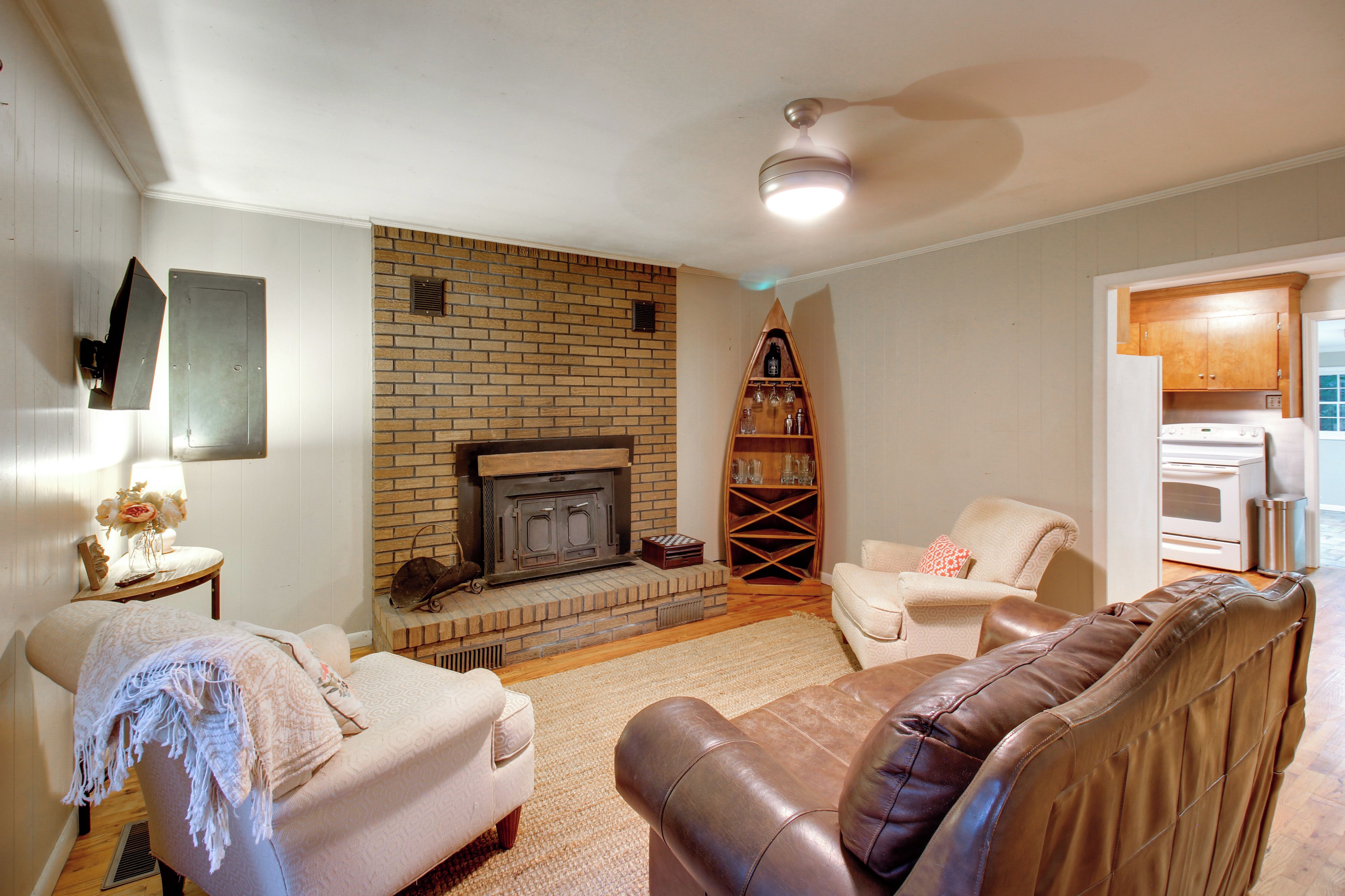 A living room with a brick fireplace, a sofa, a leather armchair, and a kitchen area with a stove.
