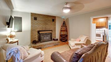 A living room with a brick fireplace, a sofa, a leather armchair, and a kitchen area with a stove.
