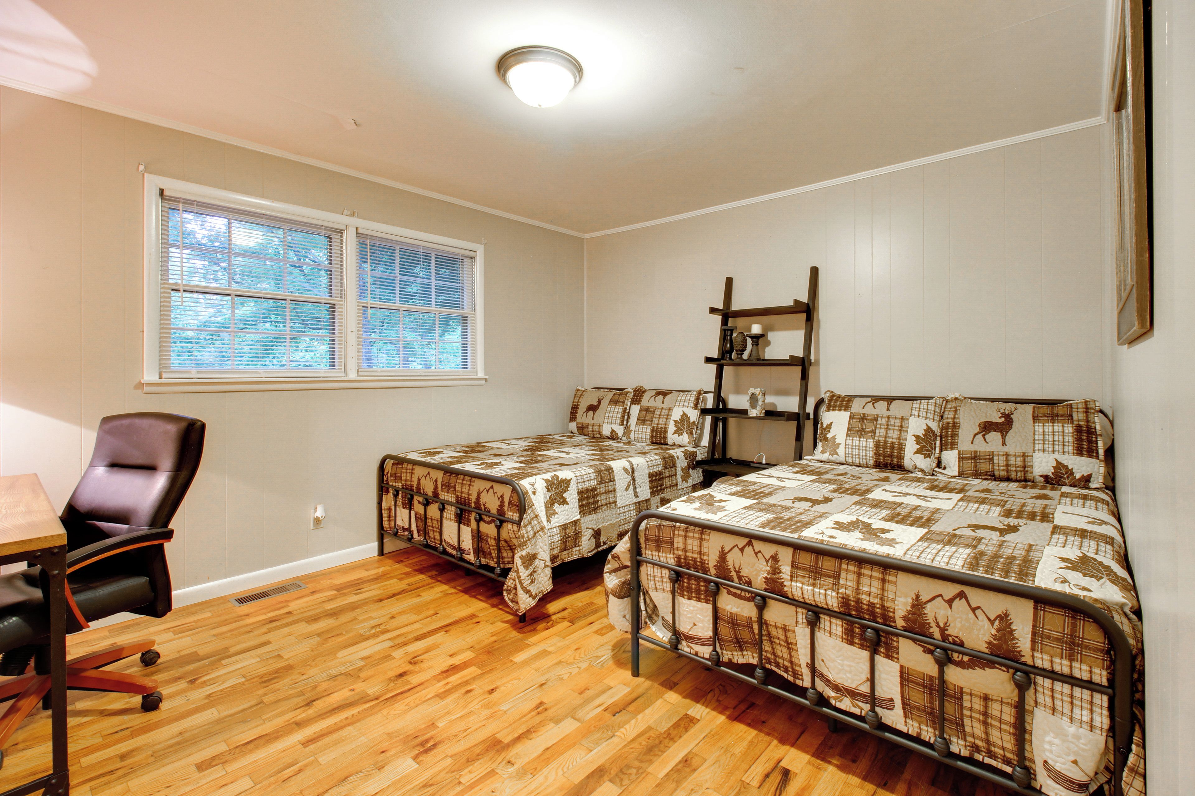 A room with two beds, a desk, a chair, and a window.