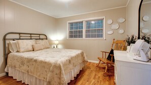 Quarto com cama, poltrona, escrivaninha com computador, janela e detalhes na parede.