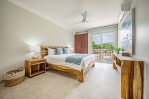 A bedroom with a bed, nightstand, and a view of greenery through a balcony. - Oceanfront Escape in Playa Potrero, Costa Rica (Tempate)