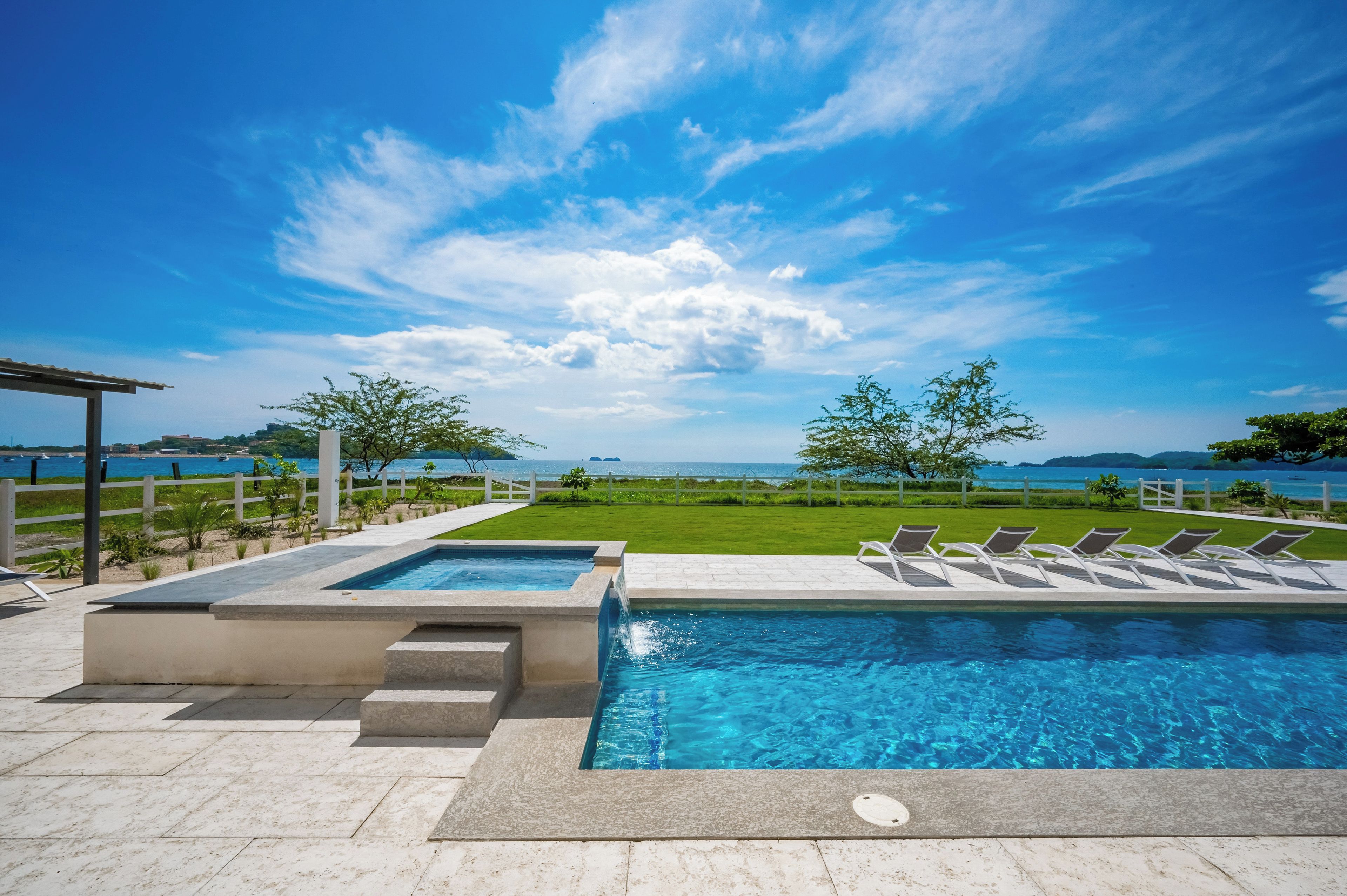 A swimming pool with a view of the sea, surrounded by a white fence and trees.