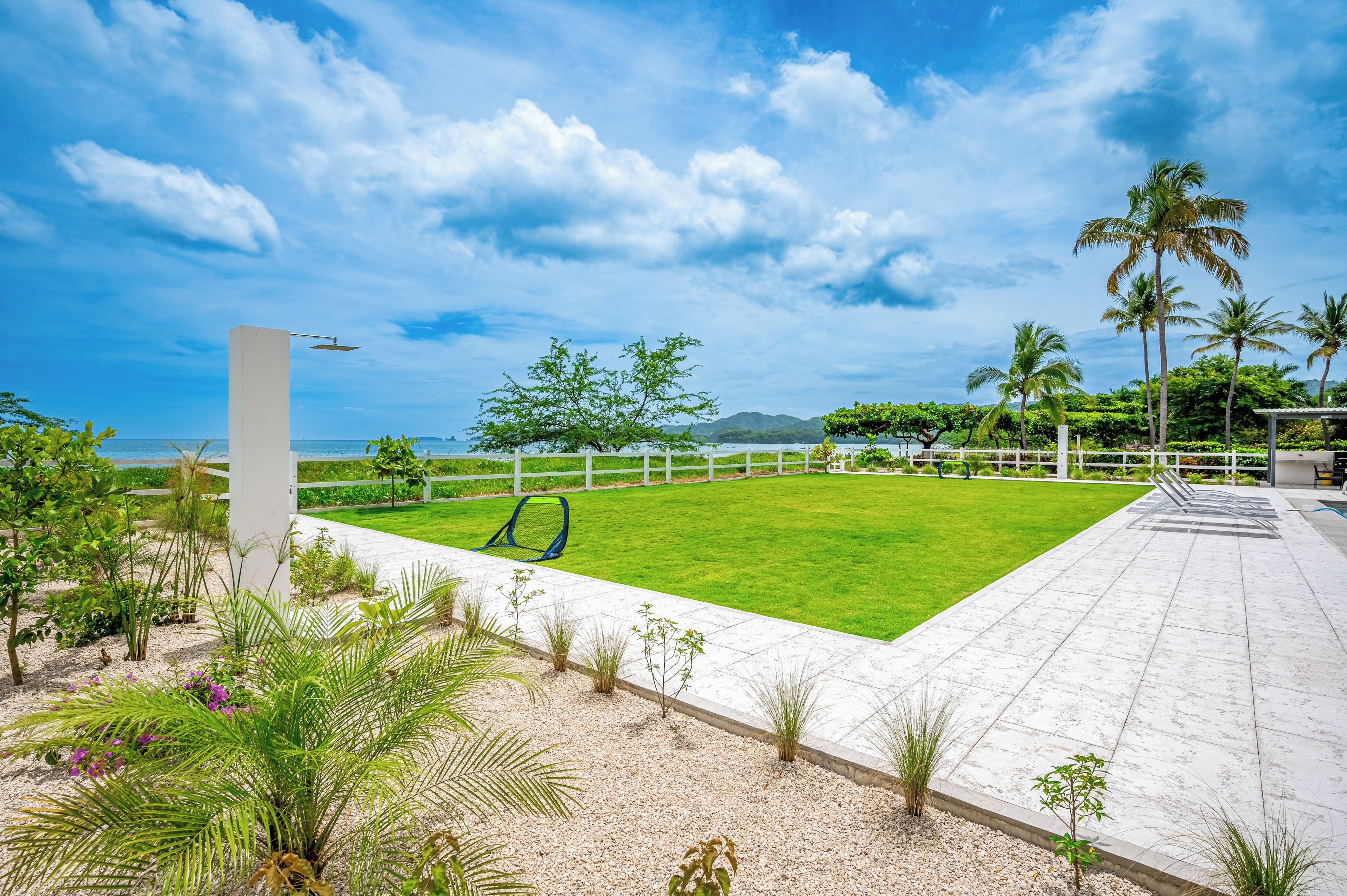 A well-maintained lawn with a seating area, a white fence, and palm trees.