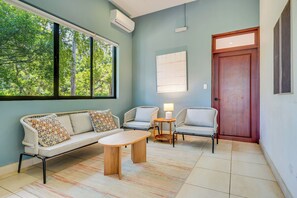 A room with a sofa, two chairs, a small table, a lamp, and a door.