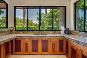 A kitchen with a large window, granite countertops, wooden cabinets, and a coffee maker.