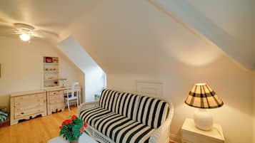 A cozy loft bedroom with a sloped ceiling, a striped sofa, a small table with a plant, a lamp, and a desk with shelves.