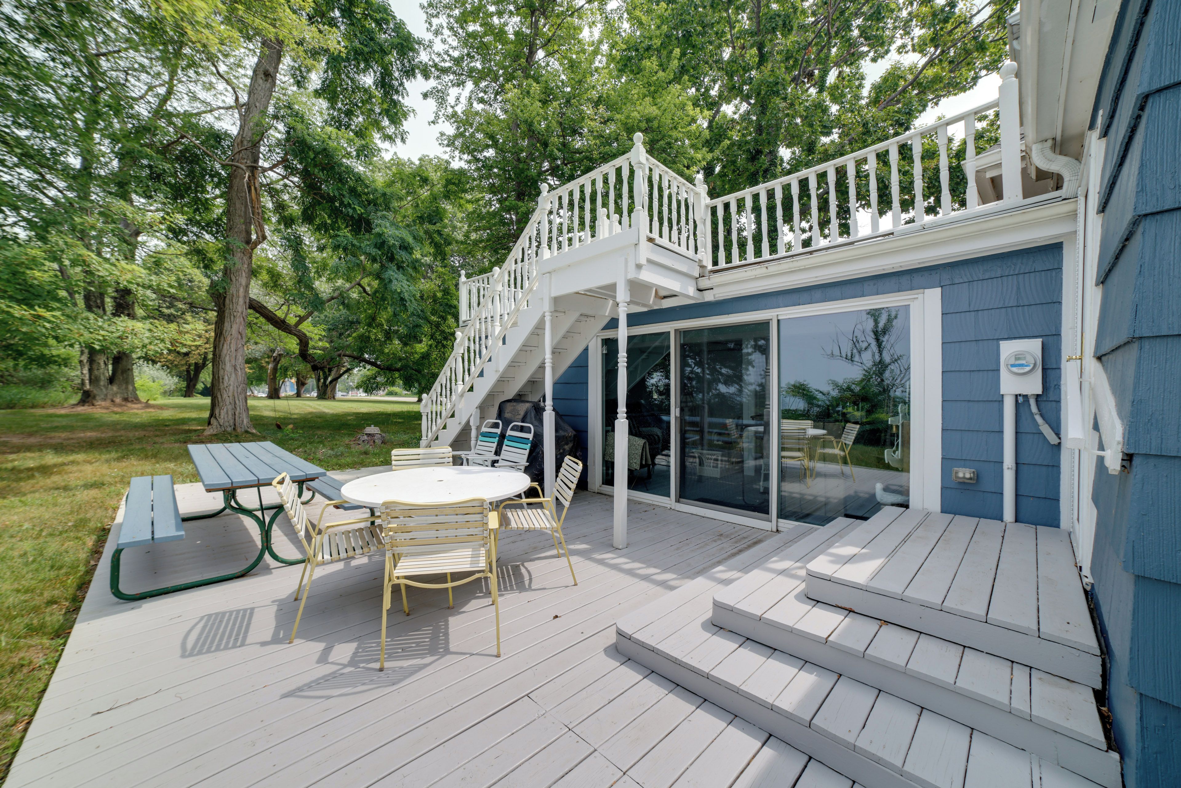 A deck with a table and chairs, a covered patio area, and a staircase leading to a balcony.