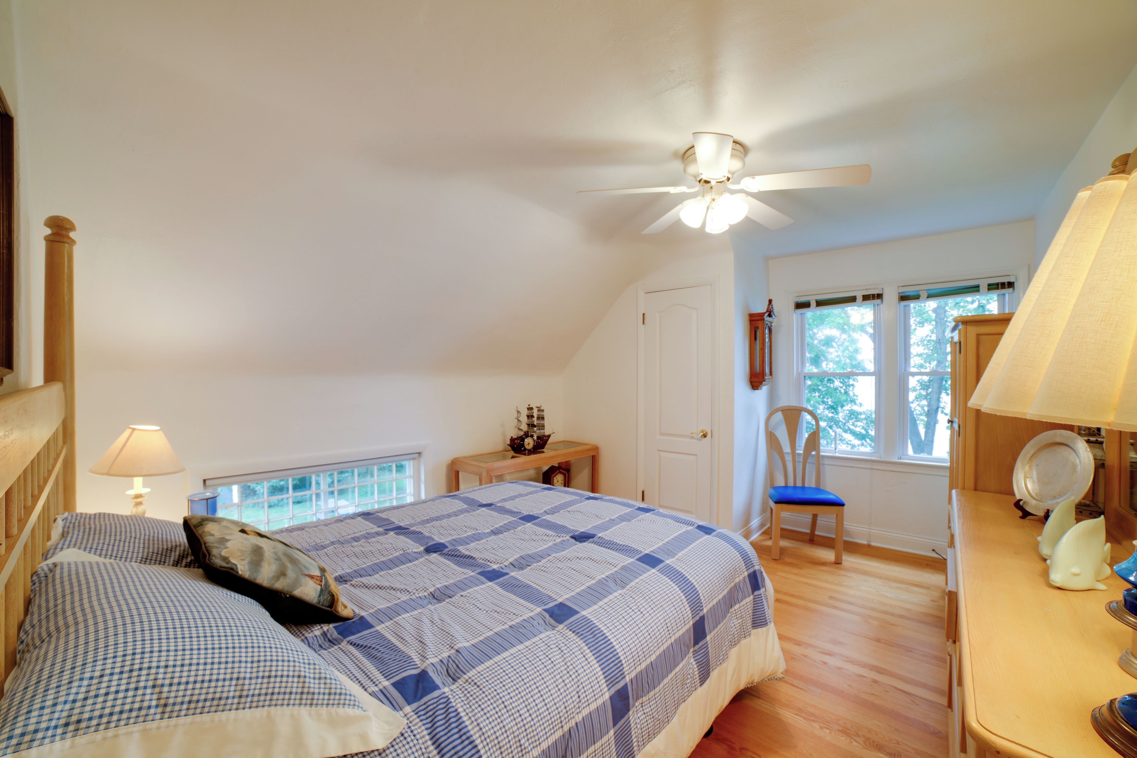 A bedroom with a bed, a nightstand, a desk, a chair, a ceiling fan, and a window.