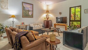 A living room with a sofa, a coffee table, a TV, and a painting on the wall. - Poolside Playa Carrillo Hideaway, Walk to Beach (Puerto Carrillo)