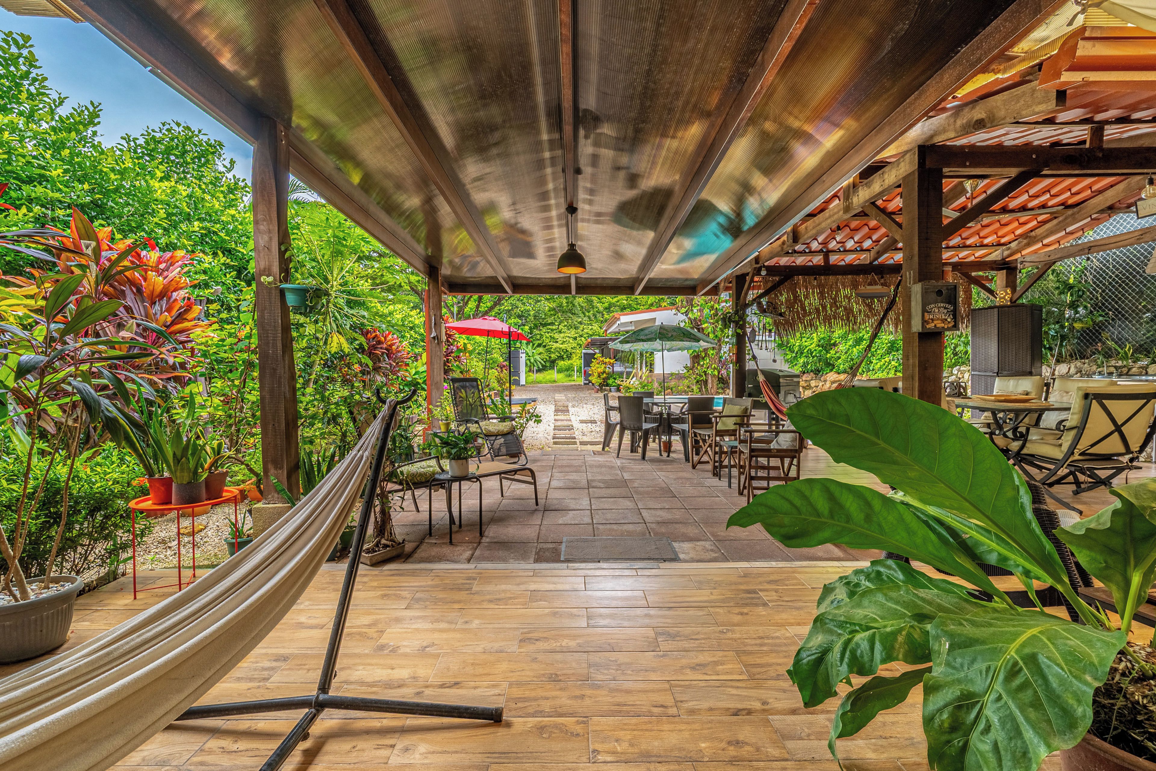 An outdoor patio area with a hammock, dining tables, chairs, and potted plants.