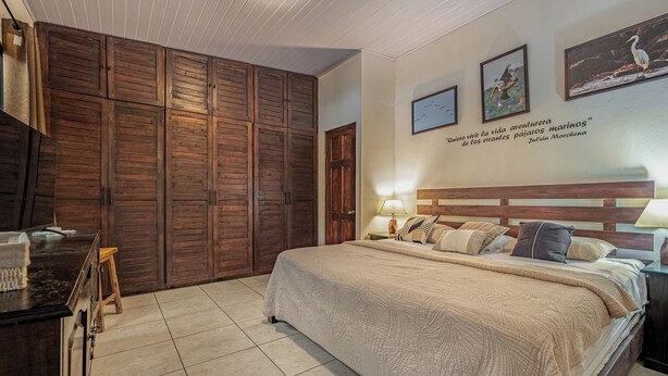 A bedroom with a large bed, wooden wardrobe, and a nightstand with a lamp. - Poolside Playa Carrillo Hideaway, Walk to Beach (Puerto Carrillo)