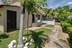 Ein Wohnhaus mit gepflasterter Auffahrt, einem kleinen Garten mit Palmen und einem weißen Gebäude mit dunkler Tür.