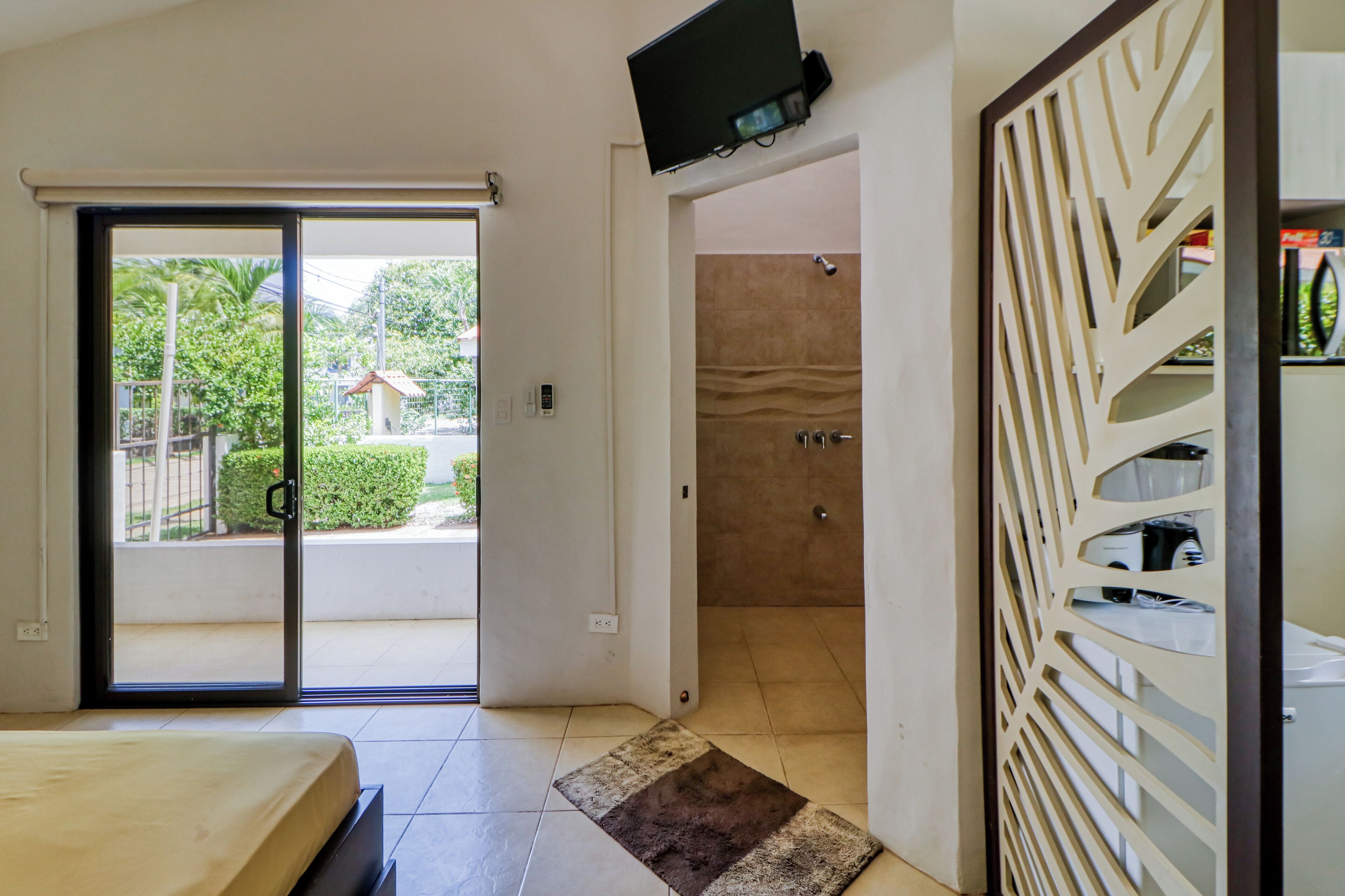 A bedroom with a bed, a shower area, and a television mounted on the wall.