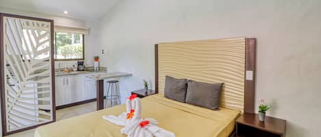 A hotel room with a bed, a nightstand, a small table, a window, and a kitchenette.