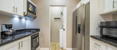 A modern kitchen with white cabinetry, a black countertop, and stainless steel appliances.