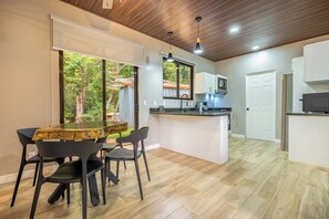 A modern kitchen with a central island, a dining area with a wooden table and chairs, and a view of the outdoors through a large window. - Shared Pool Access: Updated Apt in Playa Avellanas (Tamarindo)