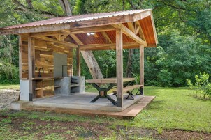 Una estructura rústica de madera con techo de metal, un lavamanos integrado y una mesa de picnic.