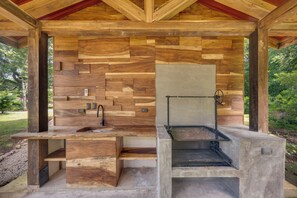 Cocina exterior con pileta y parrilla, frente a una pared de madera con encimera de hormigón.