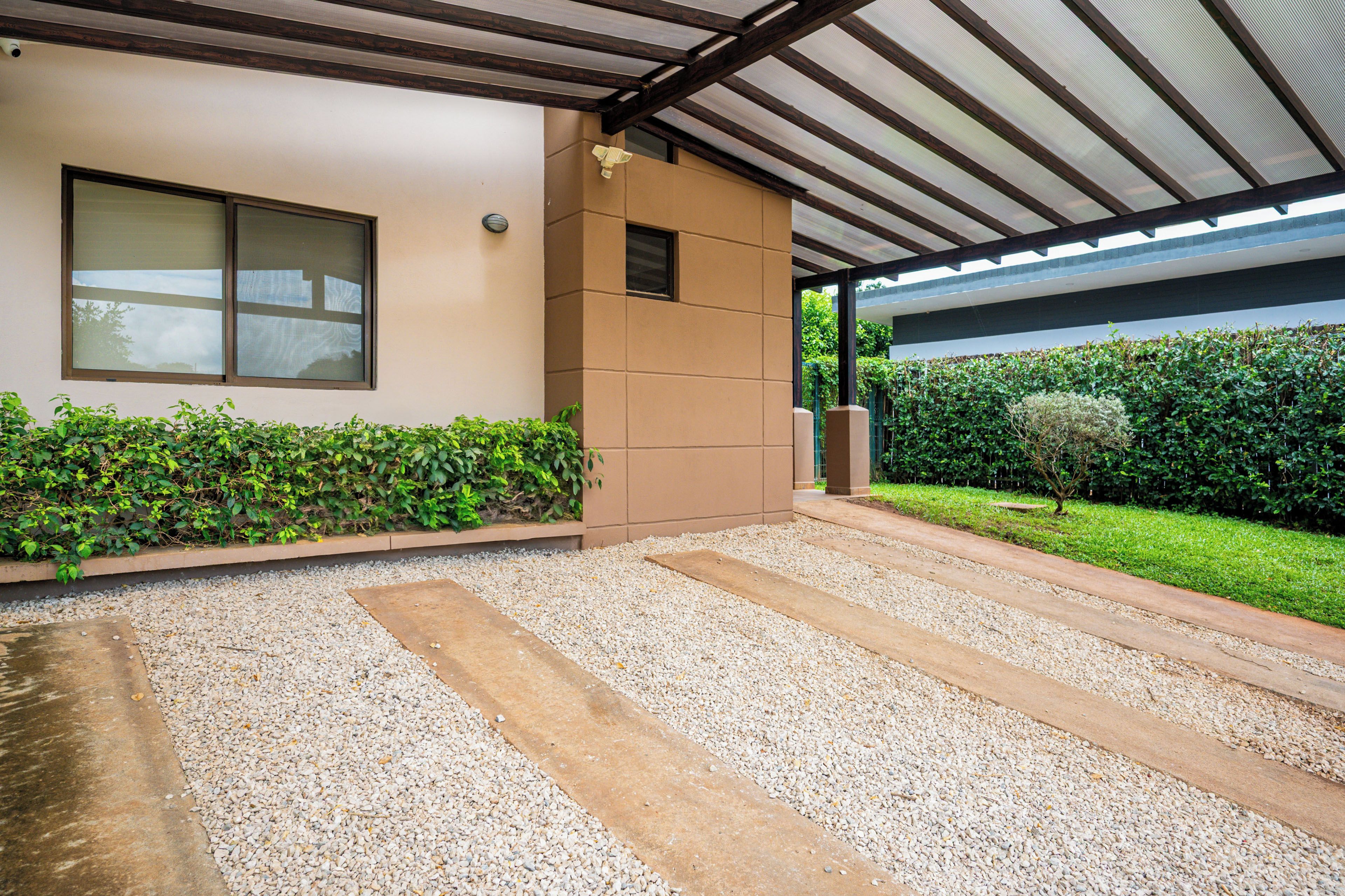 Un bâtiment moderne doté d’un patio couvert, d’un chemin de gravier et d’une haie bien entretenue.