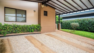 A modern building with a covered patio area, a gravel pathway, and a well-maintained hedge.