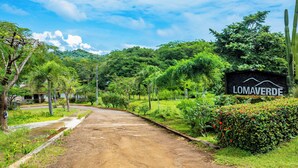 A dirt road leading to a sign with 'LOMAVERDE' written on it, surrounded by lush greenery and trees. - Modern + Spacious Tamarindo Home w/ Private Pool (Tamarindo)