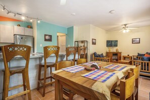 A dining area with wooden chairs and a table, a kitchen with a refrigerator, and a living room with a sofa and a television. - Resort-style Pool: Playa Ocotal Condo Near Beach! (Sardinal)