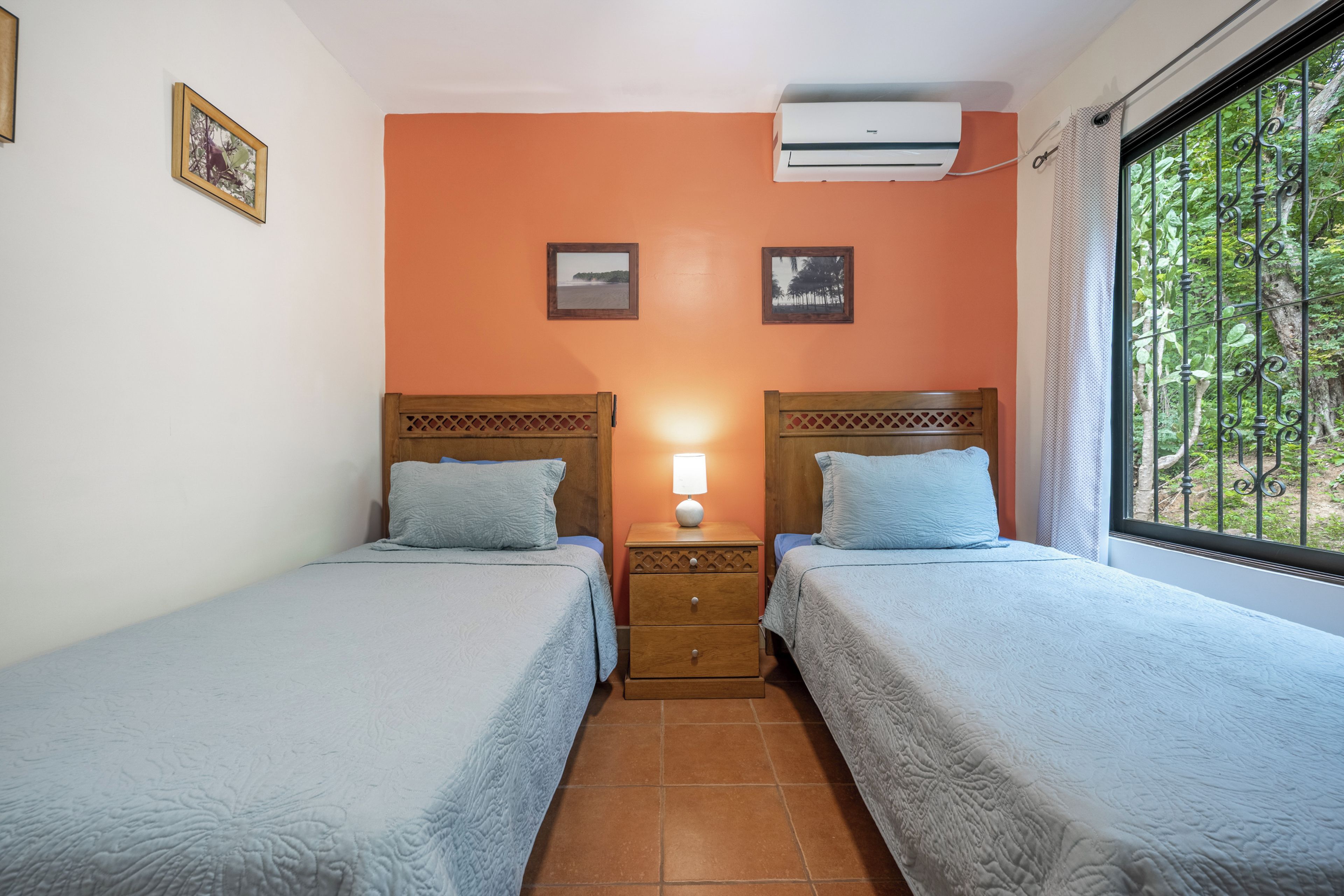 Een kamer met twee bedden, een nachtkastje, een airconditioner en een raam met uitzicht op bomen.