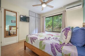 A bedroom with a bed, a ceiling fan, a TV, and a window with a view of greenery. - Resort-style Pool: Playa Ocotal Condo Near Beach! (Sardinal)