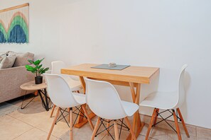 A small dining area with a wooden table and four white chairs, a potted plant, and a sofa with cushions. - 3 Mi to Beach: Modern Santa Cruz 2BR Condo (Tamarindo)