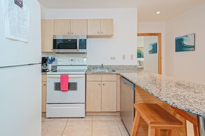 A compact kitchen with a microwave, oven, and sink. There is a wooden bench at the counter. - 3 Mi to Beach: Modern Santa Cruz 2BR Condo (Tamarindo)