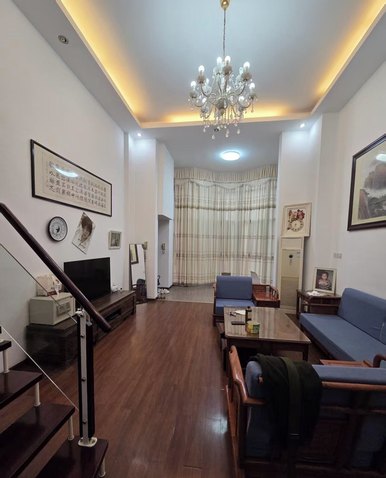 A living room with a chandelier, a sofa, a television, and a staircase.