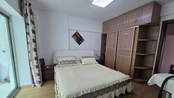 A bedroom with a bed, a wardrobe, a bedside table, and a window with curtains.