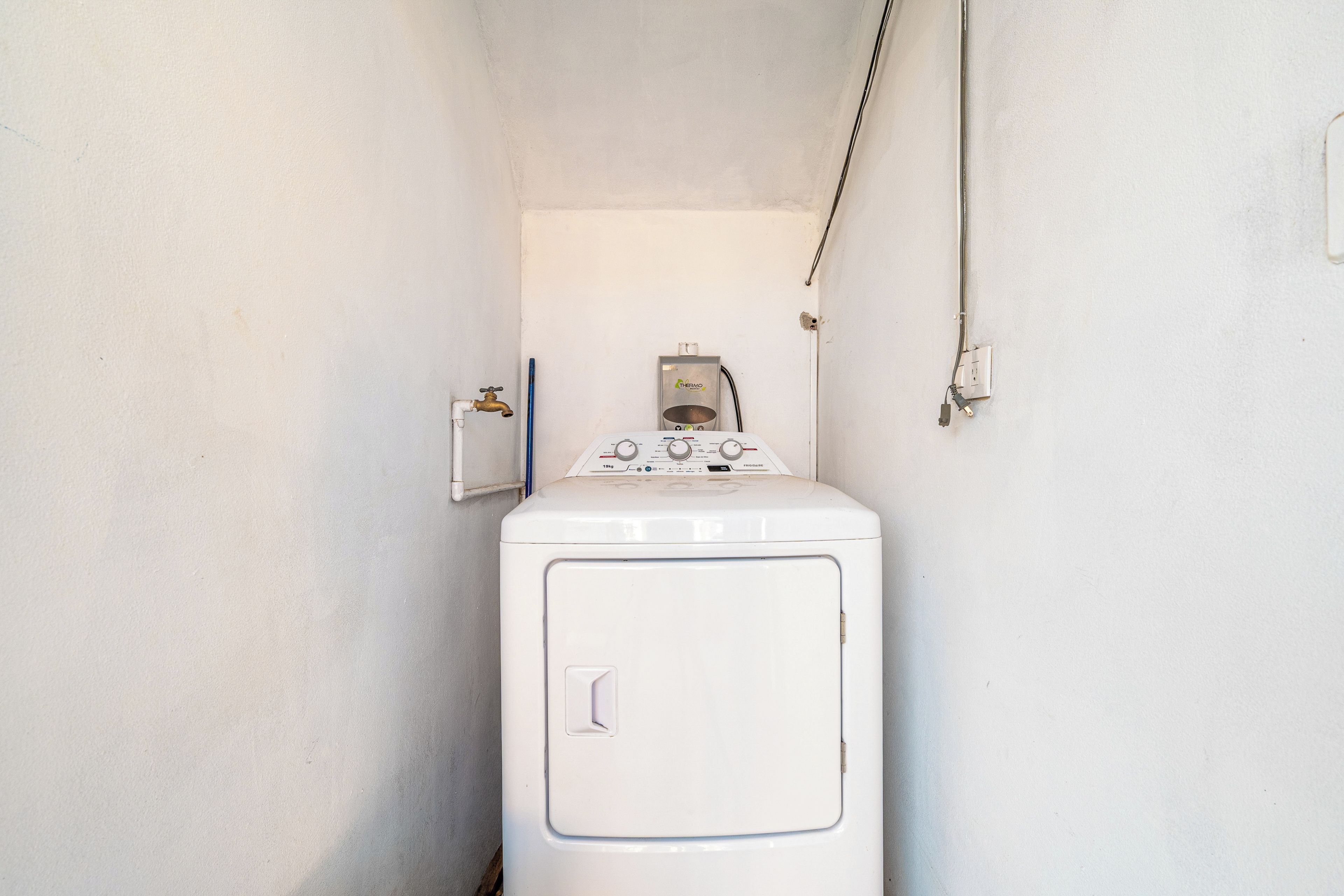 Une petite buanderie équipée d’un lave-linge à chargement frontal, d’un radiateur mural et d’une prise de courant.