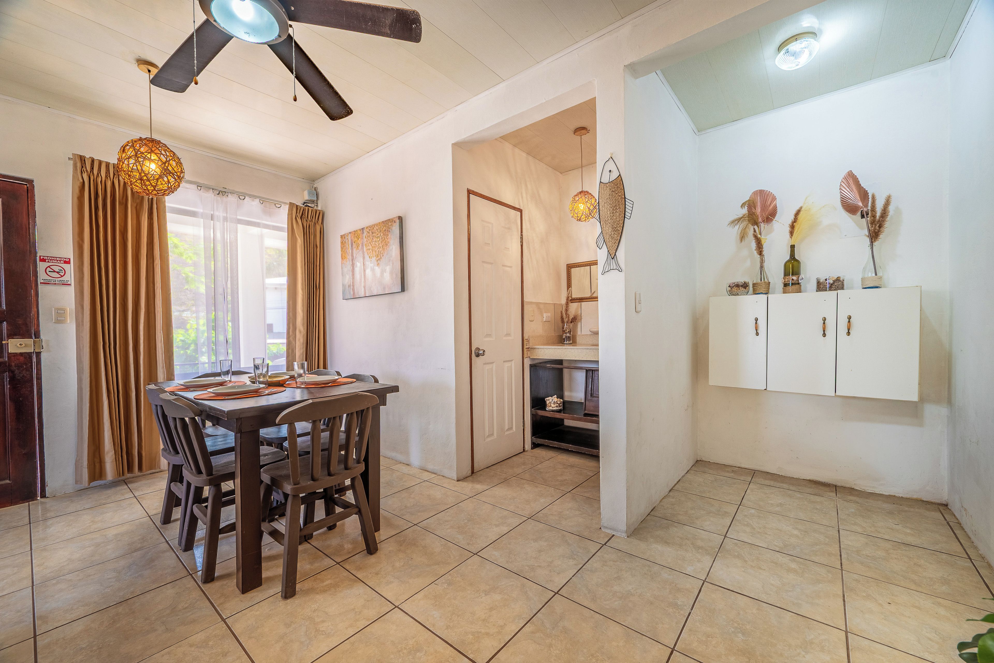 Un coin repas avec une table et des chaises en bois, un ventilateur de plafond et un meuble mural agrémenté d’objets décoratifs.