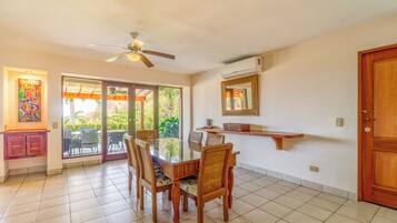 Espaço de refeições com mesa e cadeiras de vidro, ventilador de teto e vista para o exterior.