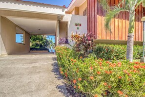 A building with a covered entrance, a garden with red flowers, and a palm tree. - Bahia Pez Vela Resort: Ocean-view Condo (Sardinal)