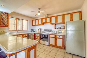 Uma cozinha com armários de madeira, geladeira, fogão e ventilador de teto.