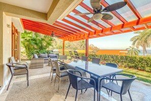 An outdoor patio with a glass table and chairs, a ceiling fan, and a view of the ocean. - Bahia Pez Vela Resort: Ocean-view Condo (Sardinal)