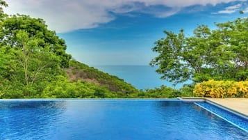 Piscina com vista para o mar e vegetação exuberante.