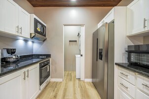 Una cocina moderna con armarios blancos, horno empotrado, microondas y refrigerador de acero inoxidable.