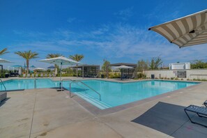 Ein Swimmingpool mit Sonnenschirm, Liegestühlen und Palmen.
